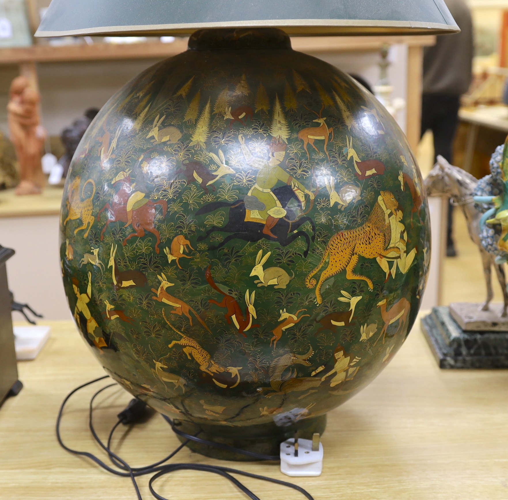 An Indian spherical green ground papier mache table lamp, decorated with hunting scenes and green shade, 75cms high including shade